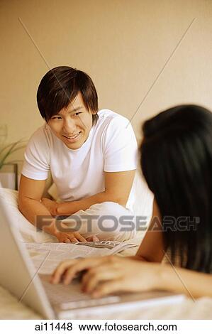 Couple in bedroom, woman using laptop and looking at man behind her. View Large Photo Image Stock Photo - Couple in bedroom, woman using laptop and looking at man behind her.. Fotosearch