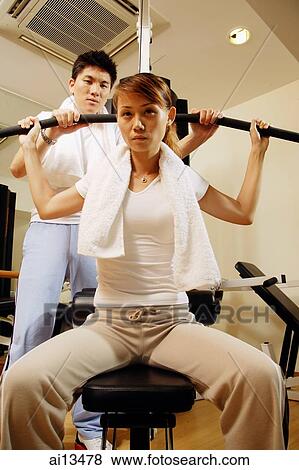 Couple in gym, man helping woman with exercise machine View Large Photo Image Stock Photo - Couple in gym, man helping woman with exercise machine. Fotosearch