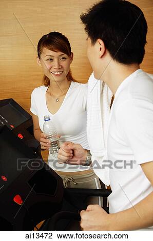 Couple in gym, man on treadmill, woman holding bottle of water looking at him View Large Photo Image Stock Image - Couple in gym, man on treadmill, woman holding bottle of water looking at him. Fotosearch