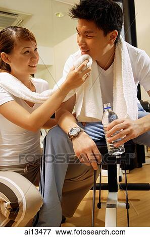 Couple in gym, resting, woman wiping man's face with towel View Large Photo Image Stock Photo - Couple in gym, resting, woman wiping man's face with towel. Fotosearch