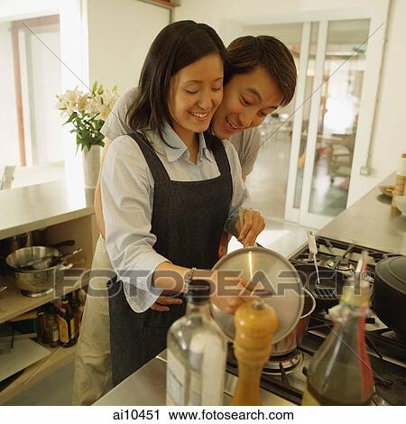 Stock Image - Couple in kitchen, man hugging woman from behind. Fotosearch