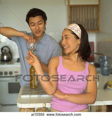 Couple in kitchen, man opening wine bottle, woman holding wine glass View Large Photo Image Stock Photography - Couple in kitchen, man opening wine bottle, woman holding wine glass. Fotosearch