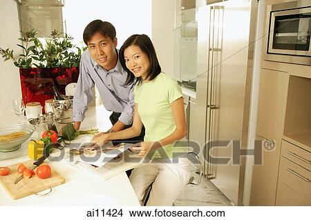 Couple in kitchen with cookbook, looking at camera View Large Photo Image Picture - Couple in kitchen with cookbook, looking at camera. Fotosearch