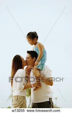 Couple kissing, daughter sitting on father's shoulder View Large Photo Image Stock Photography - Couple kissing, daughter sitting on father's shoulder. Fotosearch