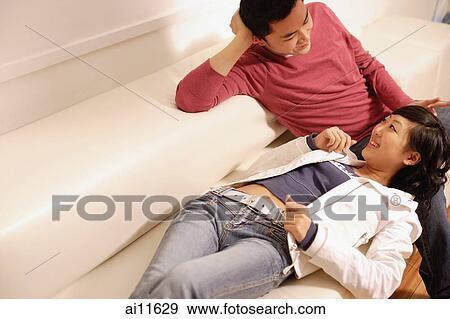 Stock Photo - Couple lounging on sofa, woman lying down on man's lap. Fotosearch