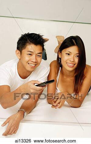 Couple lying on bed, man holding remote control View Large Photo Image Stock Photograph - Couple lying on bed, man holding remote control. Fotosearch