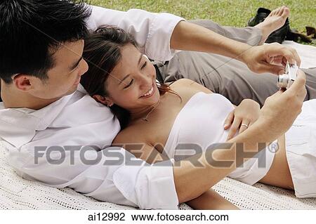Couple lying on picnic blanket, taking a picture View Large Photo Image Stock Image - Couple lying on picnic blanket, taking a picture. Fotosearch