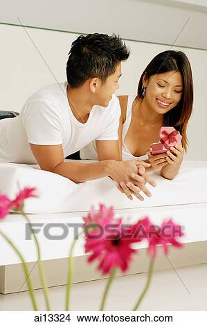 Couple lying side by side, woman holding gift box View Large Photo Image Picture - Couple lying side by side, woman holding gift box. Fotosearch