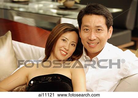 Stock Image - Couple on sofa, looking at camera. Fotosearch