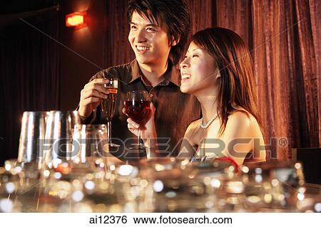 Couple side by side at night club, holding drinks View Large Photo Image Stock Photograph - Couple side by side at night club, holding drinks. Fotosearch