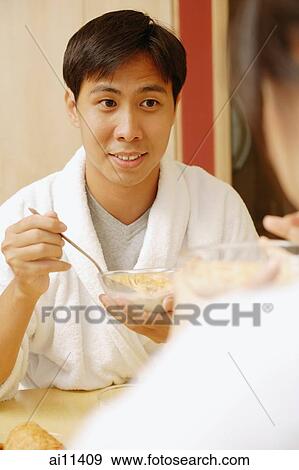 Stock Photo - Couple sitting across each other eating cereal.. Fotosearch