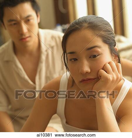 Stock Image - Couple sitting apart, woman with hand on chin. Fotosearch
