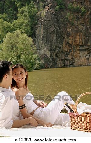 Couple sitting by a lake, with picnic basket View Large Photo Image Stock Image - Couple sitting by a lake, with picnic basket. Fotosearch
