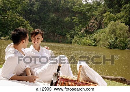 Couple sitting by a lake, with picnic basket, looking at each other View Large Photo Image Stock Image - Couple sitting by a lake, with picnic basket, looking at each other. Fotosearch