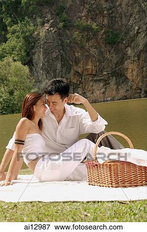 Couple sitting by a lake, with picnic basket, looking at each other View Large Photo Image Stock Photo - Couple sitting by a lake, with picnic basket, looking at each other. Fotosearch