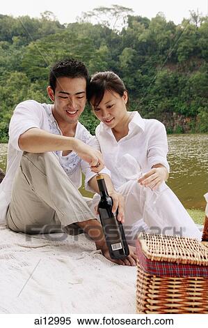 Couple sitting by a lake, with picnic basket, opening bottle of wine View Large Photo Image Stock Photography - Couple sitting by a lake, with picnic basket, opening bottle of wine. Fotosearch