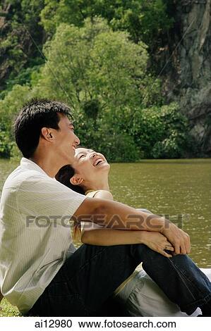 Couple sitting by lake, laughing View Large Photo Image Stock Image - Couple sitting by lake, laughing. Fotosearch