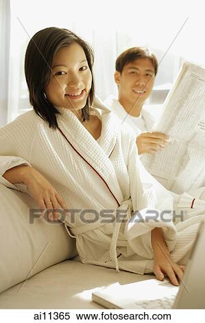 Couple sitting down, man holding newspaper, woman with hand on laptop, looking at camera View Large Photo Image Stock Photography - Couple sitting down, man holding newspaper, woman with hand on laptop, looking at camera. Fotosearch