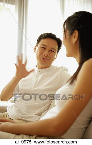 Stock Photography - Couple sitting down side by side, man with hand raised. Fotosearch