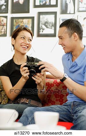 Couple sitting on sofa holding camera View Large Photo Image Stock Image - Couple sitting on sofa holding camera. Fotosearch