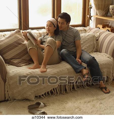 Couple sitting on sofa, looking at magazine View Large Photo Image Picture - Couple sitting on sofa, looking at magazine. Fotosearch