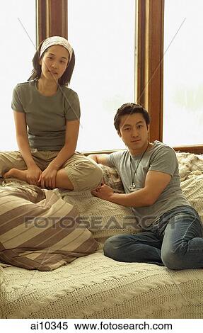 Stock Photography - Couple sitting on sofa, looking at camera. Fotosearch
