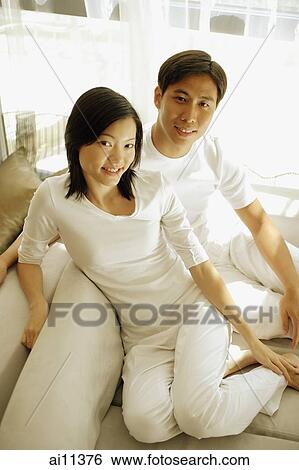 Couple sitting on sofa side by side, looking at camera View Large Photo Image Stock Photograph - Couple sitting on sofa side by side, looking at camera. Fotosearch