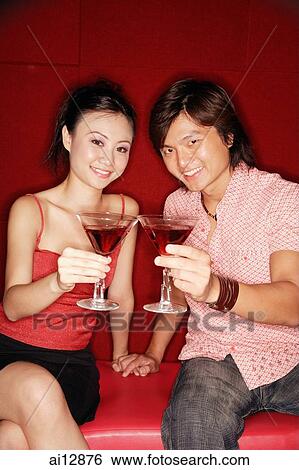 Couple sitting side by side, holding drinks, looking at camera View Large Photo Image Stock Photograph - Couple sitting side by side, holding drinks, looking at camera. Fotosearch