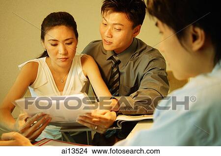 Couple sitting side by side, looking at documents, man in the foreground View Large Photo Image Picture - Couple sitting side by side, looking at documents, man in the foreground. Fotosearch