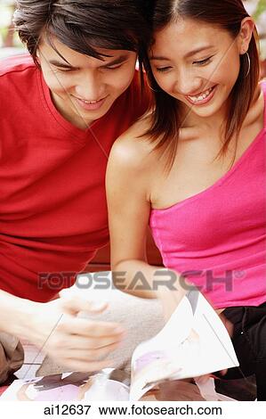 Couple sitting side by side, looking at magazine View Large Photo Image Stock Photo - Couple sitting side by side, looking at magazine. Fotosearch