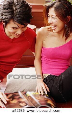 Couple sitting side by side, magazine open in front of them View Large Photo Image Stock Photograph - Couple sitting side by side, magazine open in front of them. Fotosearch