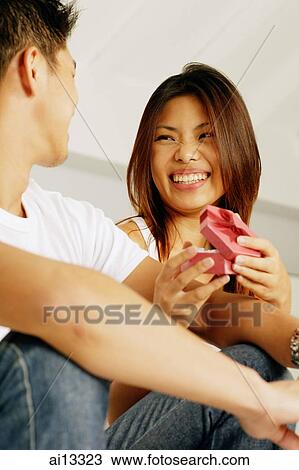 Stock Image - Couple sitting side by side, woman holding gift box. Fotosearch