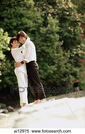 Couple standing in park, hugging, looking at camera View Large Photo Image Stock Photography - Couple standing in park, hugging, looking at camera. Fotosearch