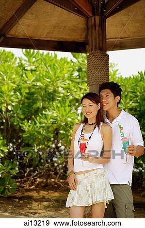 Couple standing, looking away, holding drinks View Large Photo Image Stock Photo - Couple standing, looking away, holding drinks. Fotosearch