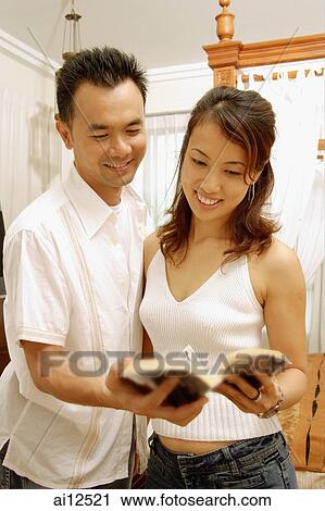 Stock Image - Couple standing side by side, looking at magazine. Fotosearch