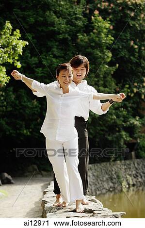 Couple walking along ledge, arms outstretched View Large Photo Image Stock Image - Couple walking along ledge, arms outstretched. Fotosearch