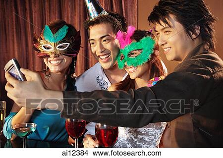 Couples with mask and hat using camera phone to take a picture View Large Photo Image Picture - Couples with mask and hat using camera phone to take a picture. Fotosearch