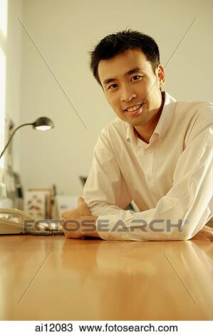 Stock Image - Executive sitting at desk, arms crossed, looking at camera. Fotosearch