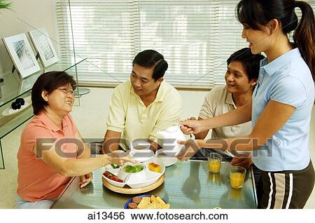 Family sitting around table, daughter pouring tea for mother View Large Photo Image Stock Photograph - Family sitting around table, daughter pouring tea for mother. Fotosearch