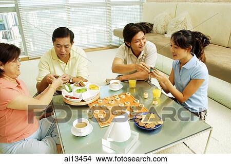 Family sitting in living room with food and board game on table in front of them. View Large Photo Image Picture - Family sitting in living room with food and board game on table in front of them.. Fotosearch