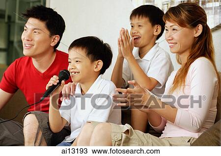 Stock Image - Family with two children in living room, son singing. Fotosearch