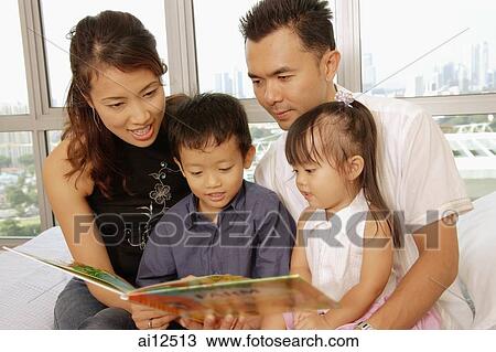 Family with two children sitting together, looking at book View Large Photo Image Stock Image - Family with two children sitting together, looking at book. Fotosearch