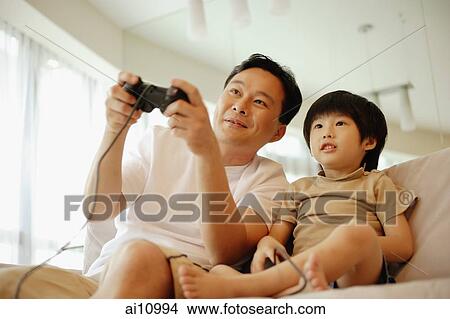 Father and son sitting on sofa, playing with video game, low angle view View Large Photo Image Picture - Father and son sitting on sofa, playing with video game, low angle view. Fotosearch