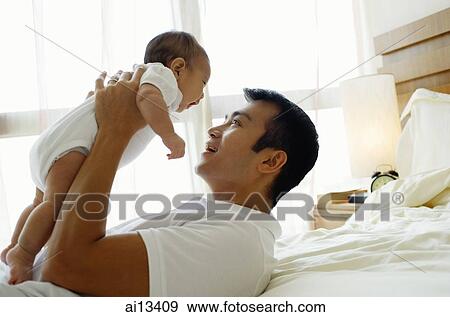 Father carrying baby daughter, lying on bed View Large Photo Image Stock Photo - Father carrying baby daughter, lying on bed. Fotosearch