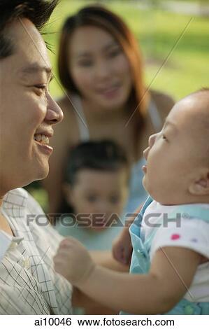 Stock Photograph - Father carrying baby, mother and young daughter in the background.. Fotosearch