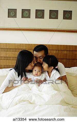 Picture - Father, mother and daughter kissing baby daughter. Fotosearch