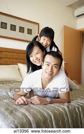 Father, mother and daughter lying on bed, looking at camera View Large Photo Image Stock Photograph - Father, mother and daughter lying on bed, looking at camera. Fotosearch