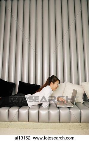 Female executive using laptop, lying on sofa View Large Photo Image Stock Image - Female executive using laptop, lying on sofa. Fotosearch