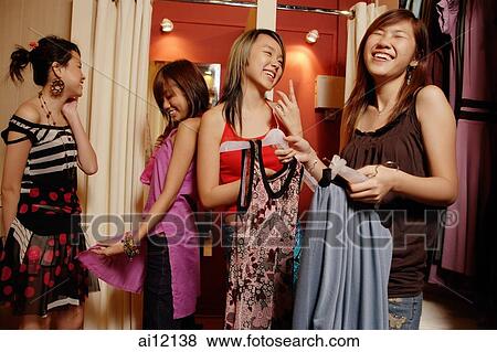 Stock Photo - Four young women at shop, looking at and trying on clothes. Fotosearch
