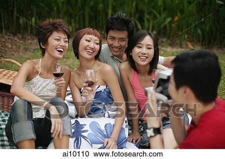 Stock Image - Friends posing for pictures, holding wine glasses. Fotosearch